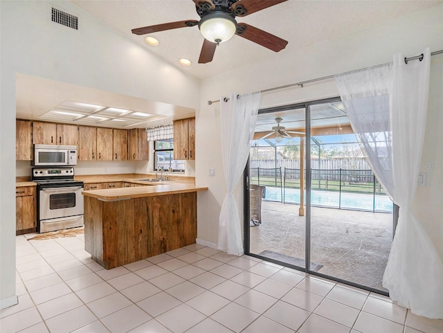 kitchen featuring stainless steel electric stove, vaulted ceiling, kitchen peninsula, light tile patterned floors, and sink