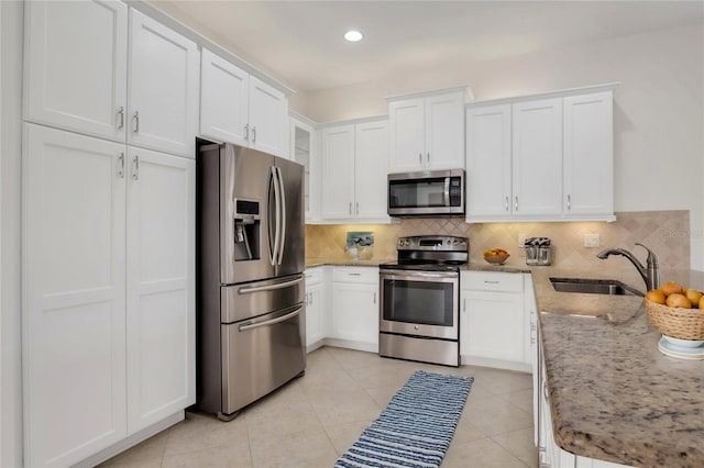 kitchen featuring white cabinetry, stainless steel appliances, decorative backsplash, light stone countertops, and sink