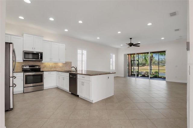 kitchen with ceiling fan, kitchen peninsula, white cabinetry, stainless steel appliances, and dark stone counters