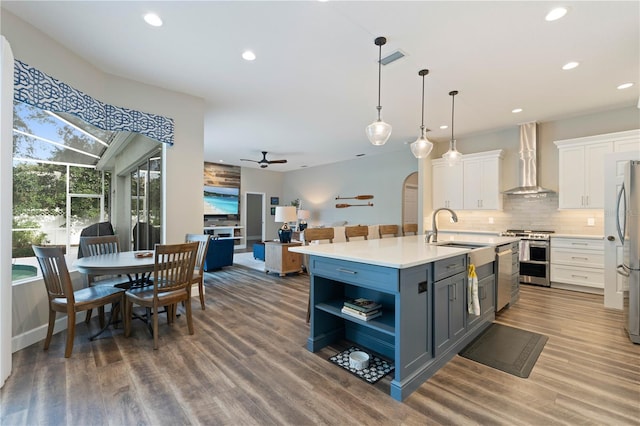 kitchen featuring sink, white cabinets, wall chimney exhaust hood, a center island with sink, and appliances with stainless steel finishes