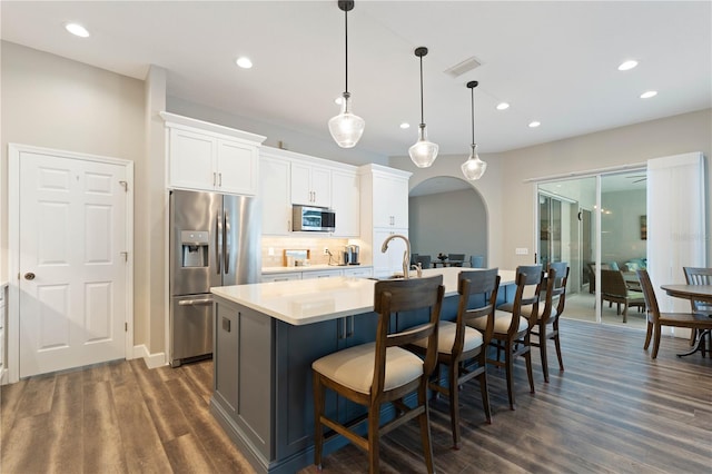 kitchen featuring white cabinets, a breakfast bar area, hanging light fixtures, a kitchen island with sink, and appliances with stainless steel finishes