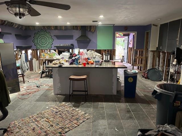 kitchen with ceiling fan, a kitchen breakfast bar, and wall chimney exhaust hood