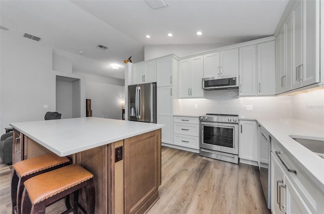 kitchen with lofted ceiling, a kitchen bar, stainless steel appliances, decorative backsplash, and white cabinets