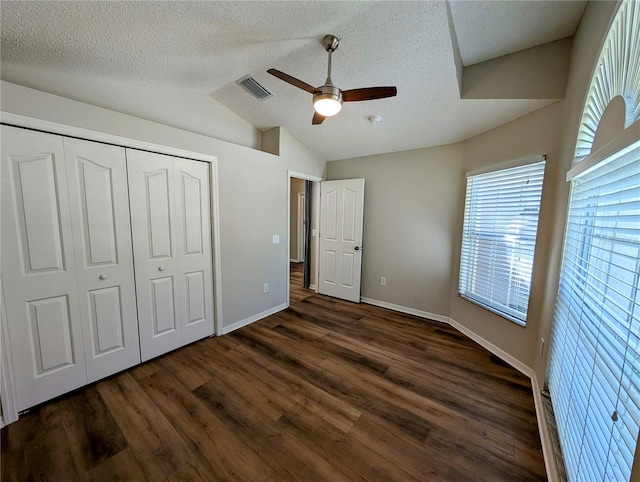 unfurnished bedroom featuring dark hardwood / wood-style floors, lofted ceiling, ceiling fan, a textured ceiling, and a closet