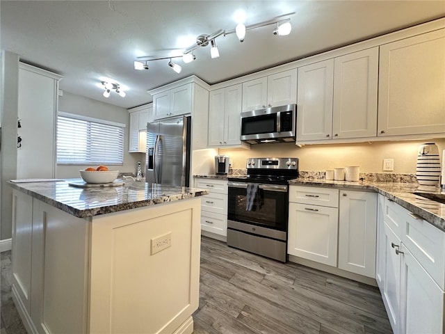 kitchen featuring a kitchen island, white cabinetry, light wood-type flooring, stainless steel appliances, and light stone counters