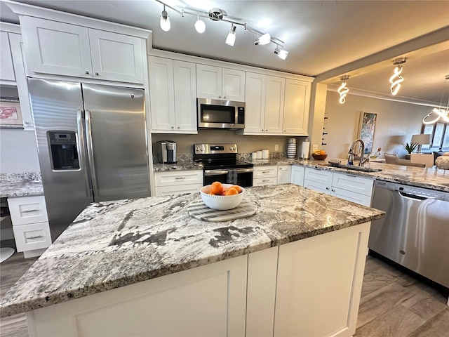 kitchen with kitchen peninsula, stainless steel appliances, light stone countertops, white cabinets, and sink