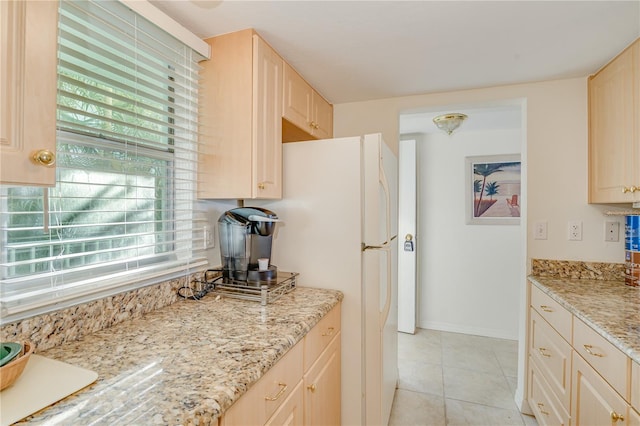 kitchen with a wealth of natural light, light stone counters, white refrigerator, and light tile patterned floors