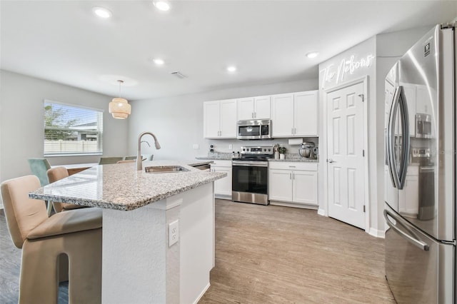 kitchen with white cabinets, stainless steel appliances, a breakfast bar, pendant lighting, and sink