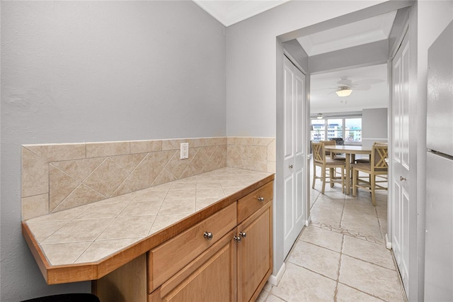 interior space featuring light tile patterned flooring, ceiling fan, stainless steel refrigerator, tile countertops, and ornamental molding