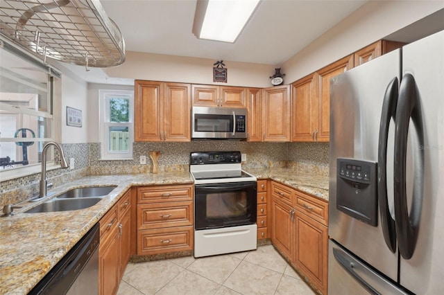 kitchen with tasteful backsplash, sink, light stone countertops, appliances with stainless steel finishes, and light tile patterned floors