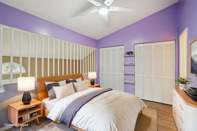 bedroom with multiple closets, vaulted ceiling, ceiling fan, and light wood-type flooring