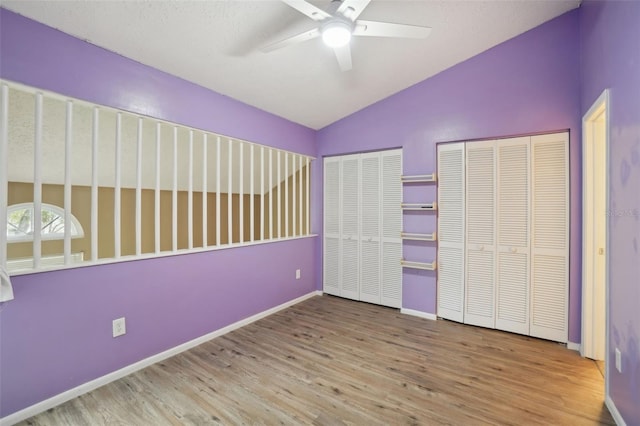 unfurnished bedroom featuring multiple closets, ceiling fan, vaulted ceiling, and light wood-type flooring