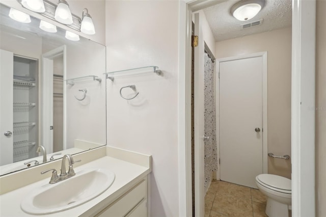 bathroom with toilet, a textured ceiling, walk in shower, tile patterned floors, and vanity