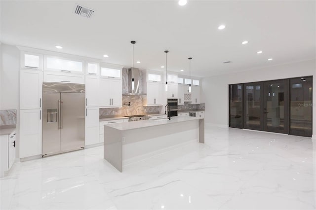 kitchen with a center island with sink, stainless steel built in fridge, white cabinetry, wall chimney range hood, and decorative light fixtures