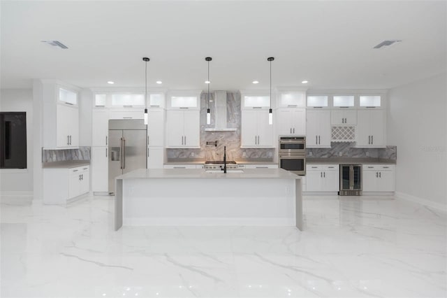 kitchen with stainless steel appliances, decorative light fixtures, white cabinets, beverage cooler, and wall chimney range hood