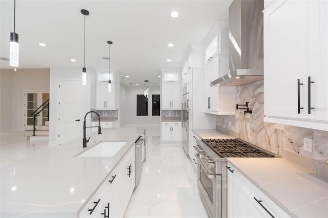 kitchen with high quality appliances, decorative light fixtures, wall chimney range hood, white cabinets, and sink