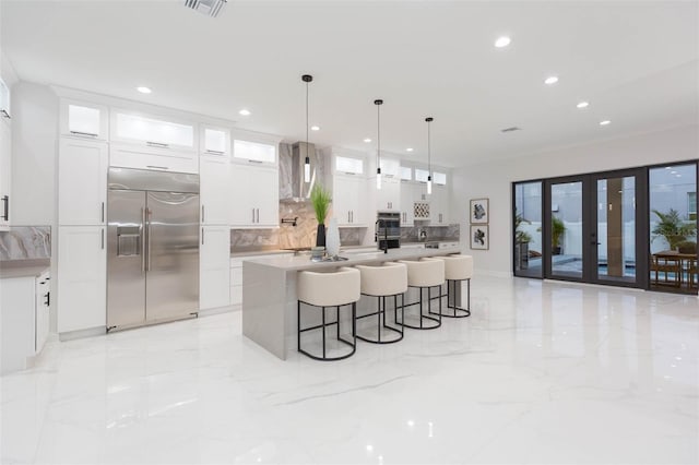 716 S Lois Ave, Tampa, FL 33609 - kitchen featuring appliances with stainless steel finishes, light marble finish floors, tasteful backsplash, a kitchen island with sink, and a breakfast bar