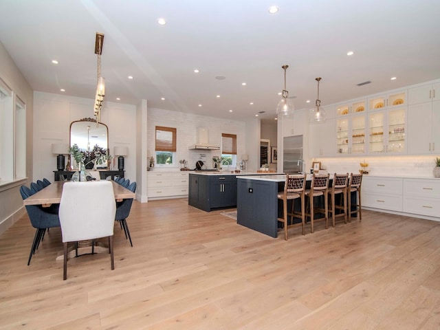 kitchen with a spacious island, white cabinetry, stainless steel built in refrigerator, light hardwood / wood-style floors, and hanging light fixtures