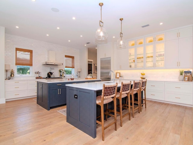 kitchen featuring wall chimney exhaust hood, a large island with sink, stainless steel built in fridge, and a breakfast bar