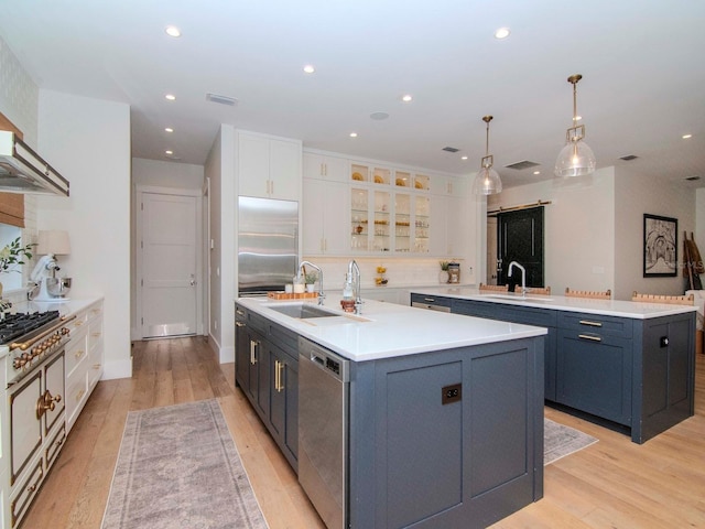 kitchen with white cabinets, pendant lighting, stainless steel appliances, and a center island with sink