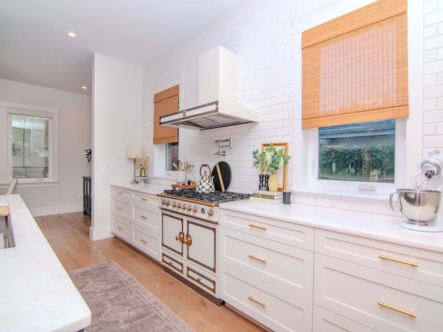 kitchen with stainless steel gas stovetop, white cabinetry, light hardwood / wood-style floors, backsplash, and wall chimney exhaust hood