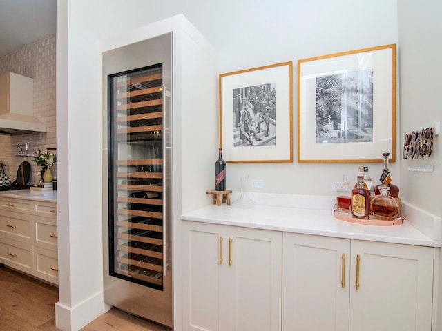 bar with tasteful backsplash, white cabinets, beverage cooler, and light hardwood / wood-style flooring