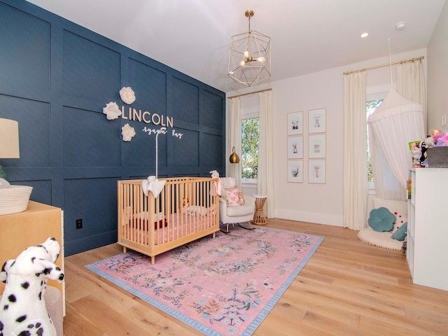 bedroom featuring light wood-type flooring, a nursery area, and a notable chandelier