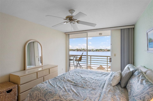 bedroom with a water view, ceiling fan, expansive windows, a textured ceiling, and access to outside