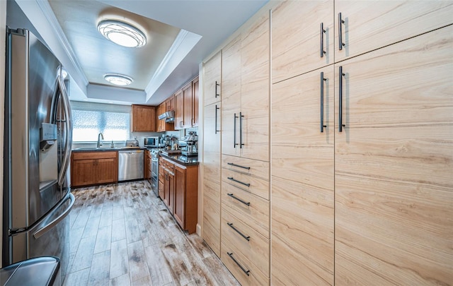 kitchen with stainless steel appliances, sink, a raised ceiling, ornamental molding, and light hardwood / wood-style flooring