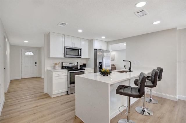 kitchen with sink, white cabinets, kitchen peninsula, a breakfast bar, and appliances with stainless steel finishes