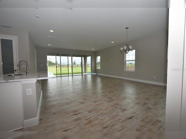 unfurnished living room with light hardwood / wood-style flooring, a chandelier, and sink