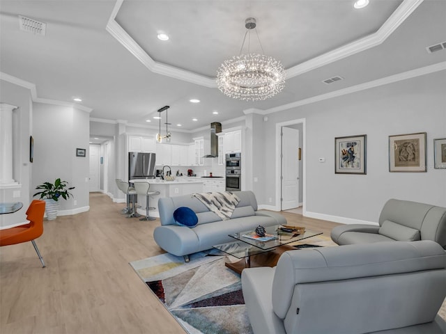 living room with crown molding, an inviting chandelier, light hardwood / wood-style flooring, and a raised ceiling