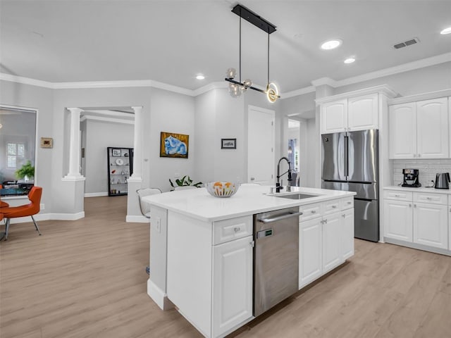 kitchen featuring pendant lighting, white cabinetry, an island with sink, decorative columns, and stainless steel appliances