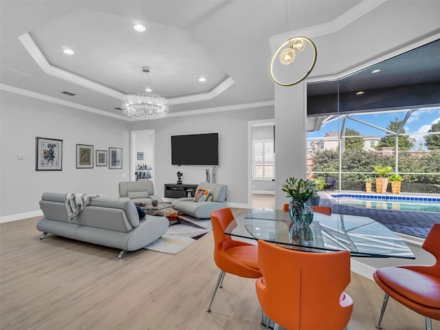 living room featuring a chandelier, a raised ceiling, light hardwood / wood-style flooring, and crown molding