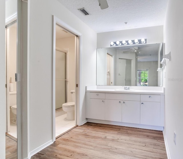 bathroom featuring toilet, vanity, hardwood / wood-style flooring, a textured ceiling, and an enclosed shower