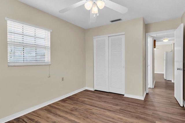 unfurnished bedroom featuring ceiling fan, dark wood-type flooring, a closet, and white fridge