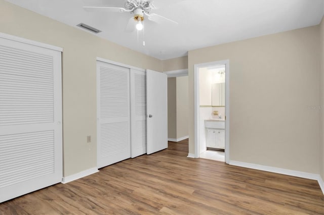 unfurnished bedroom featuring ceiling fan, wood-type flooring, connected bathroom, and two closets