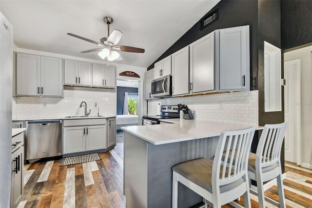 kitchen featuring stainless steel appliances, vaulted ceiling, gray cabinets, and kitchen peninsula