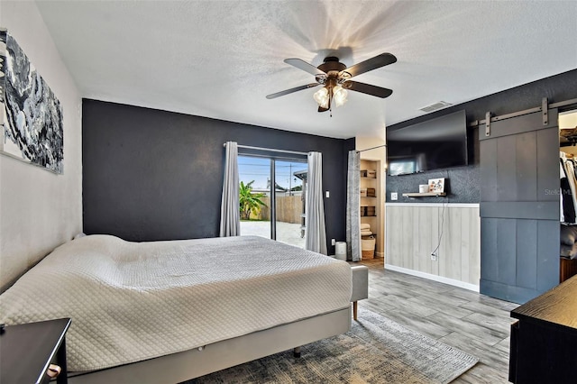 bedroom with a textured ceiling, ceiling fan, a barn door, and access to exterior