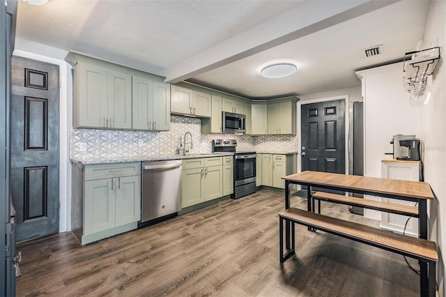 kitchen with green cabinetry, backsplash, appliances with stainless steel finishes, wood-type flooring, and sink