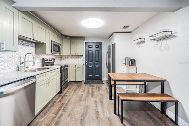 kitchen with light stone counters, green cabinetry, backsplash, appliances with stainless steel finishes, and sink