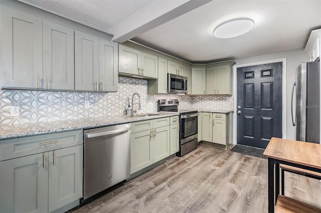 kitchen featuring stainless steel appliances, sink, light wood-type flooring, tasteful backsplash, and light stone countertops