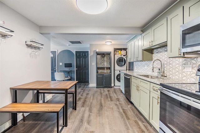 kitchen with stacked washing maching and dryer, stainless steel appliances, light stone counters, sink, and backsplash