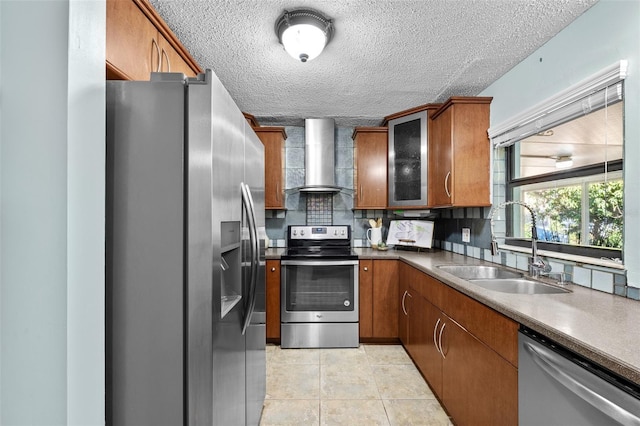 kitchen featuring wall chimney range hood, tasteful backsplash, appliances with stainless steel finishes, light tile patterned flooring, and sink