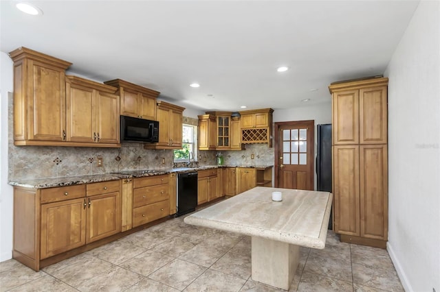 kitchen with light stone countertops, black appliances, tasteful backsplash, a kitchen island, and sink