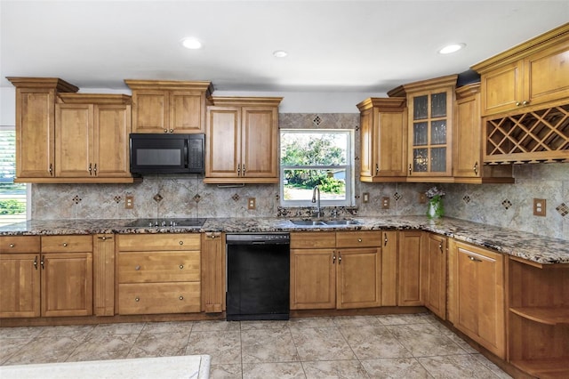 kitchen featuring black appliances, a healthy amount of sunlight, dark stone counters, and sink