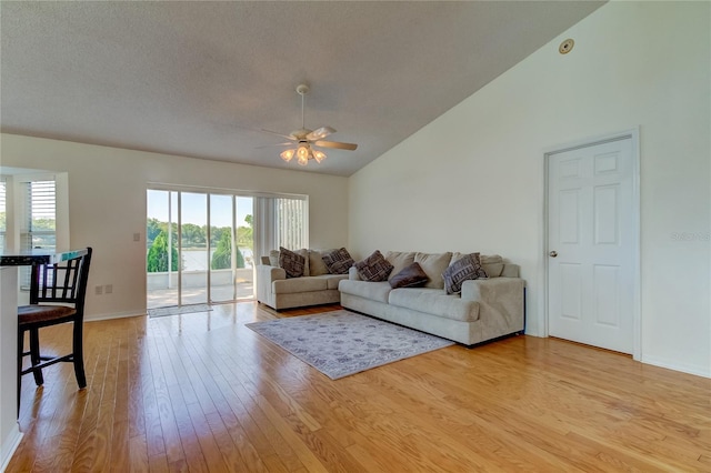 living room with vaulted ceiling, a textured ceiling, ceiling fan, and light hardwood / wood-style floors