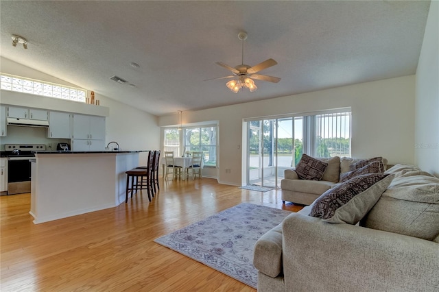 living room with lofted ceiling, a textured ceiling, ceiling fan, and light hardwood / wood-style floors