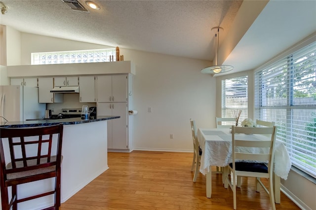 dining space featuring a textured ceiling, vaulted ceiling, and light hardwood / wood-style flooring