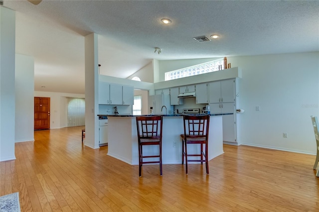 kitchen with a textured ceiling, a kitchen bar, light wood-type flooring, high vaulted ceiling, and white refrigerator with ice dispenser